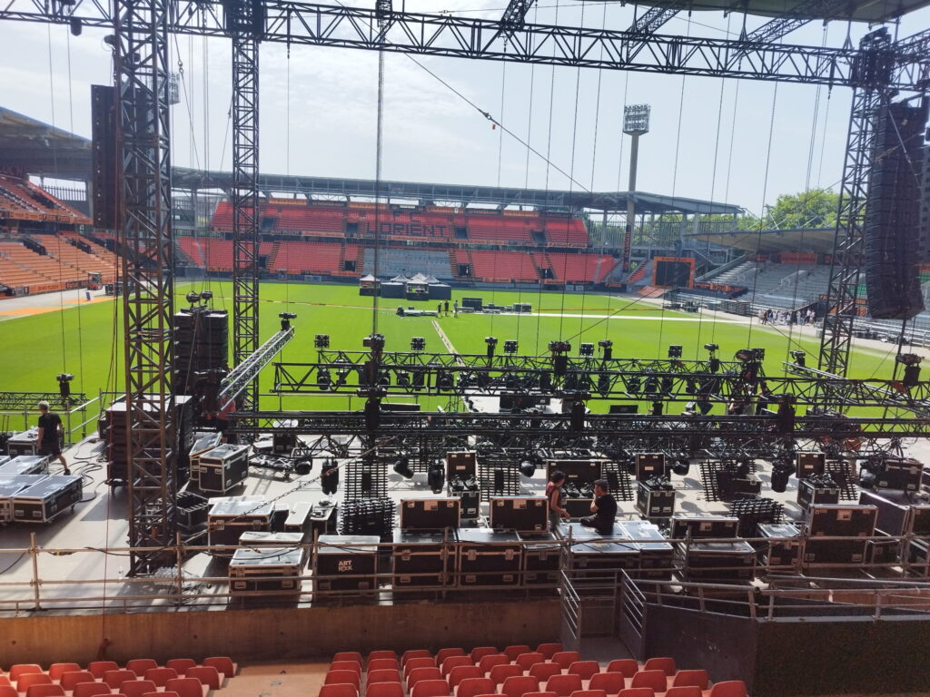 Montage de la scène du festival Art Rock au stade de Lorient avec structures treillis, flight cases et systèmes d'éclairage scénique en cours d'installation – Revolt Location