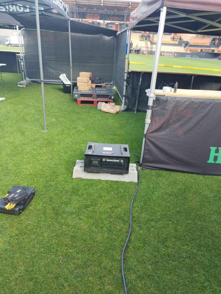 Coffret de distribution électrique événementiel posé sur dalle béton sur la pelouse du stade de Lorient lors d'un montage – location matériel électrique Revolt Location