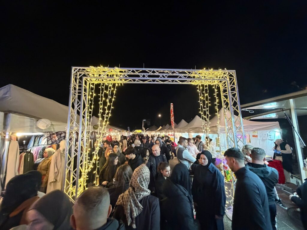 Portique en aluminium orné de guirlandes lumineuses dorées Revolt Location, marquant l'entrée d'un marché nocturne fréquenté.
