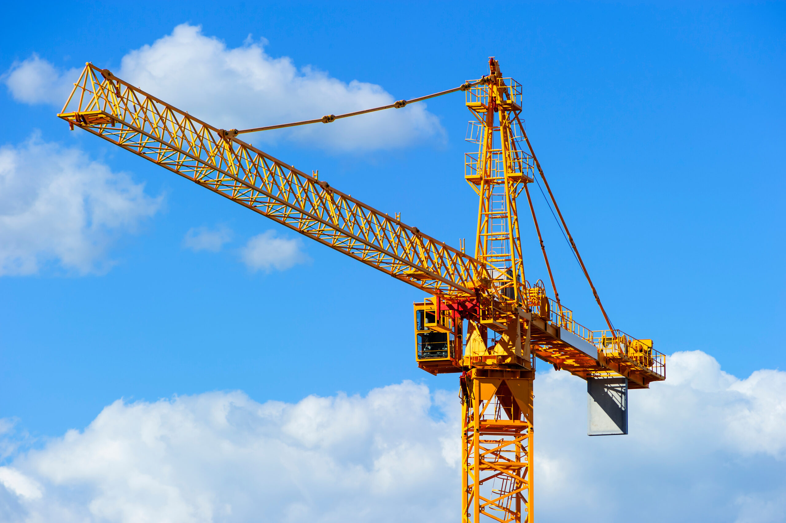 Grue à tour jaune sur chantier BTP se découpant sur un ciel bleu – secteur d'intervention Revolt Location
