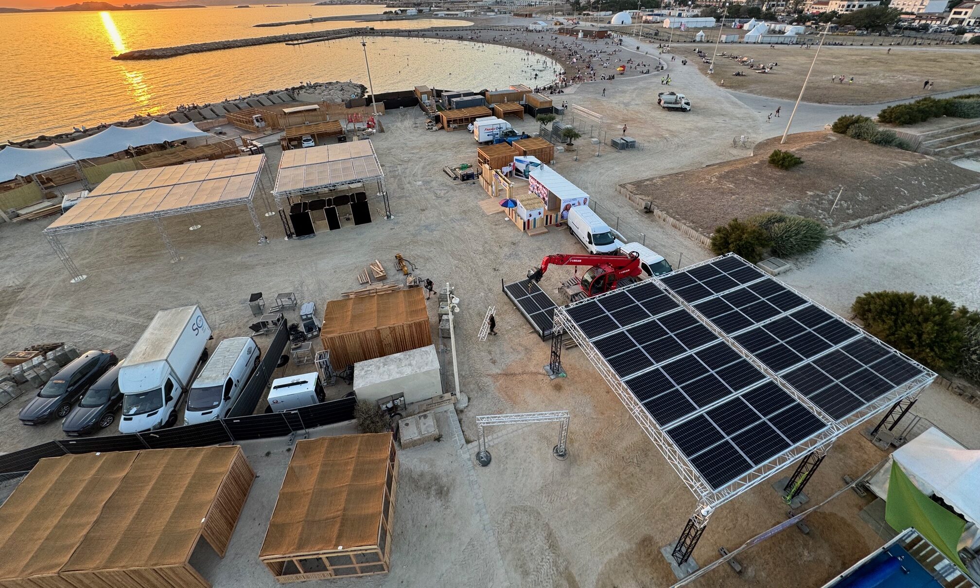 Vue aérienne d'ombrières photovoltaïques Revolt Location sur structure aluminium, installées sur un site événementiel en bord de plage au coucher du soleil.