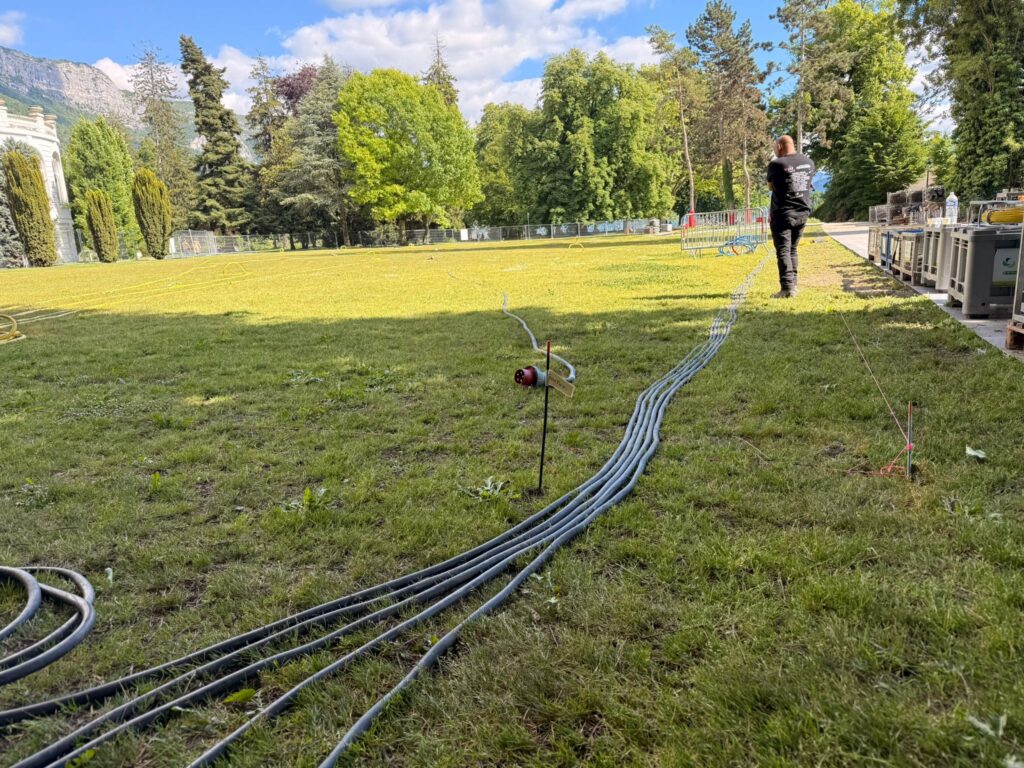 Technicien Revolt Location tirant des câbles électriques industriels sur une pelouse lors du montage d'un événement en plein air à Annecy – déploiement électrique événementiel en espace vert