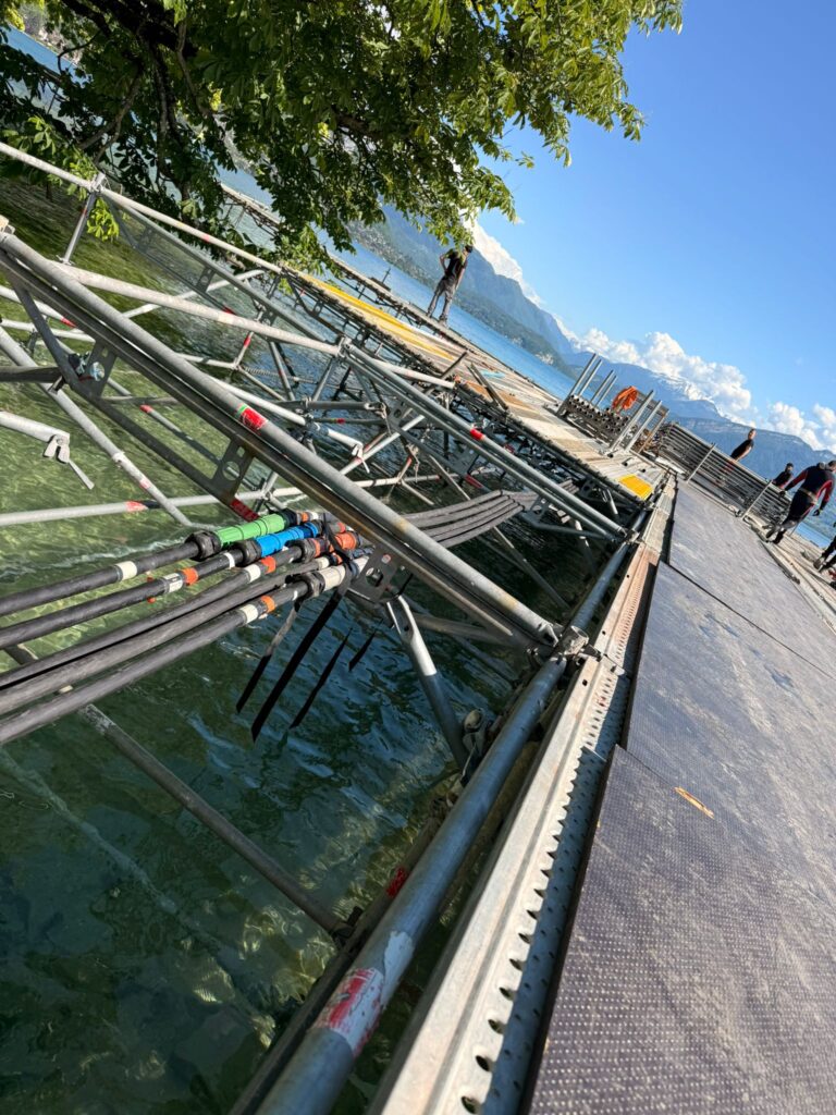 Câbles électriques industriels multicolores fixés sous la structure métallique immergée d'une scène flottante sur le lac d'Annecy – câblage événementiel en milieu aquatique Revolt Location