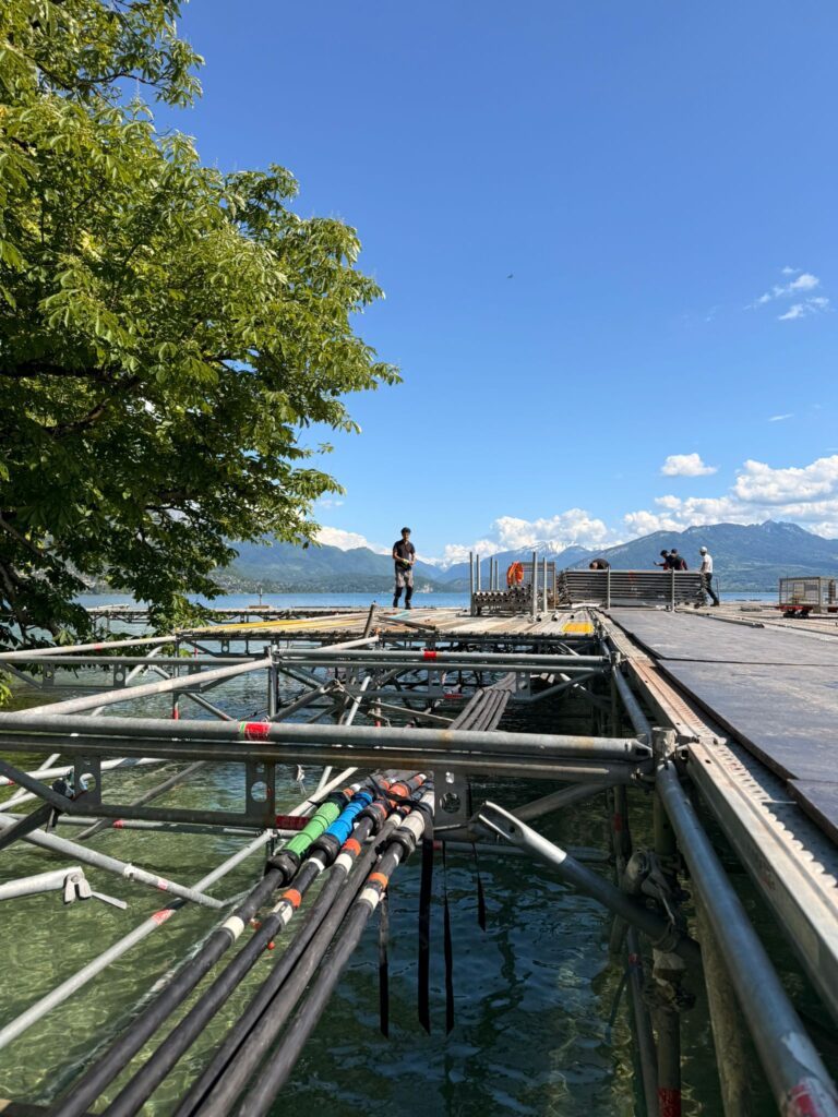 Câbles électriques multicolores fixés sous une structure de scène flottante sur le lac d'Annecy lors du montage du Festival d'Animation d'Annecy – installation électrique événementielle Revolt Location