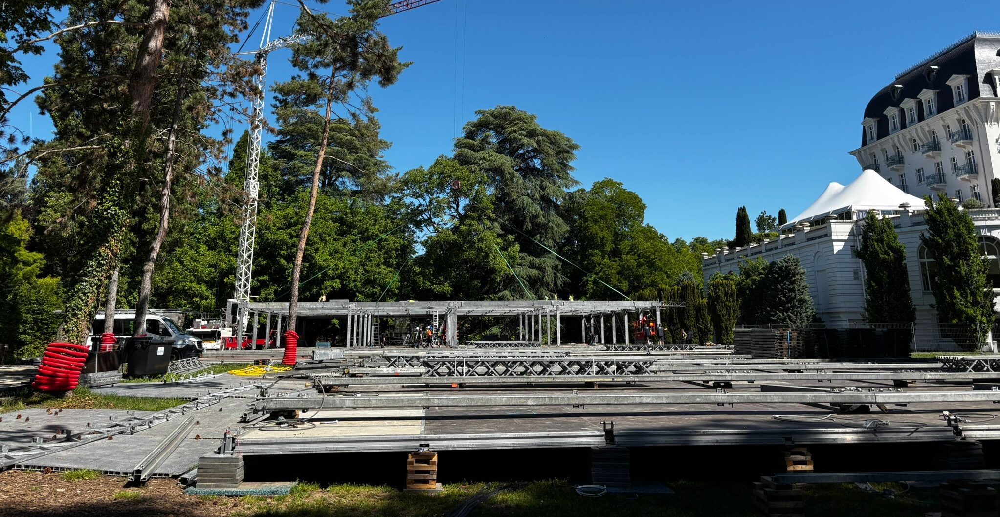 Vue d'ensemble du chantier de montage événementiel en plein air avec grue et structures aluminium au pied d'un bâtiment haussmannien