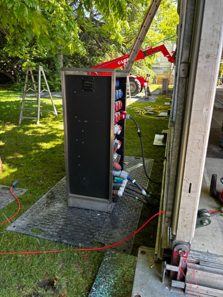 Armoire de distribution électrique événementielle avec prises industrielles CEE raccordées, installée en extérieur sur dalle antidérapante lors d'un montage en jardin – Revolt Location