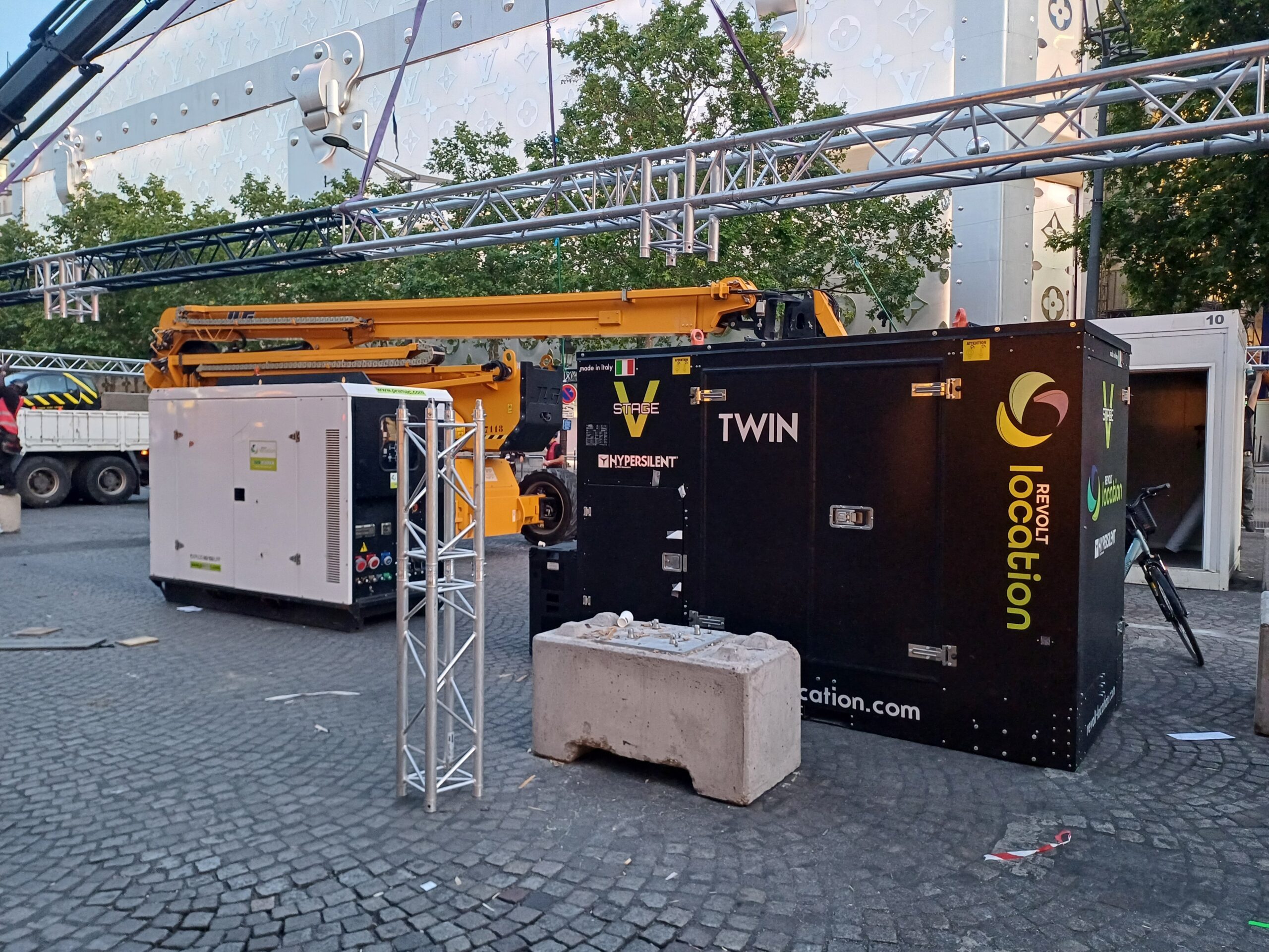 Groupe électrogène Stage V Twin Revolt Location installé sur un montage scénique urbain, avec nacelle élévatrice et structure de trusses en arrière-plan.