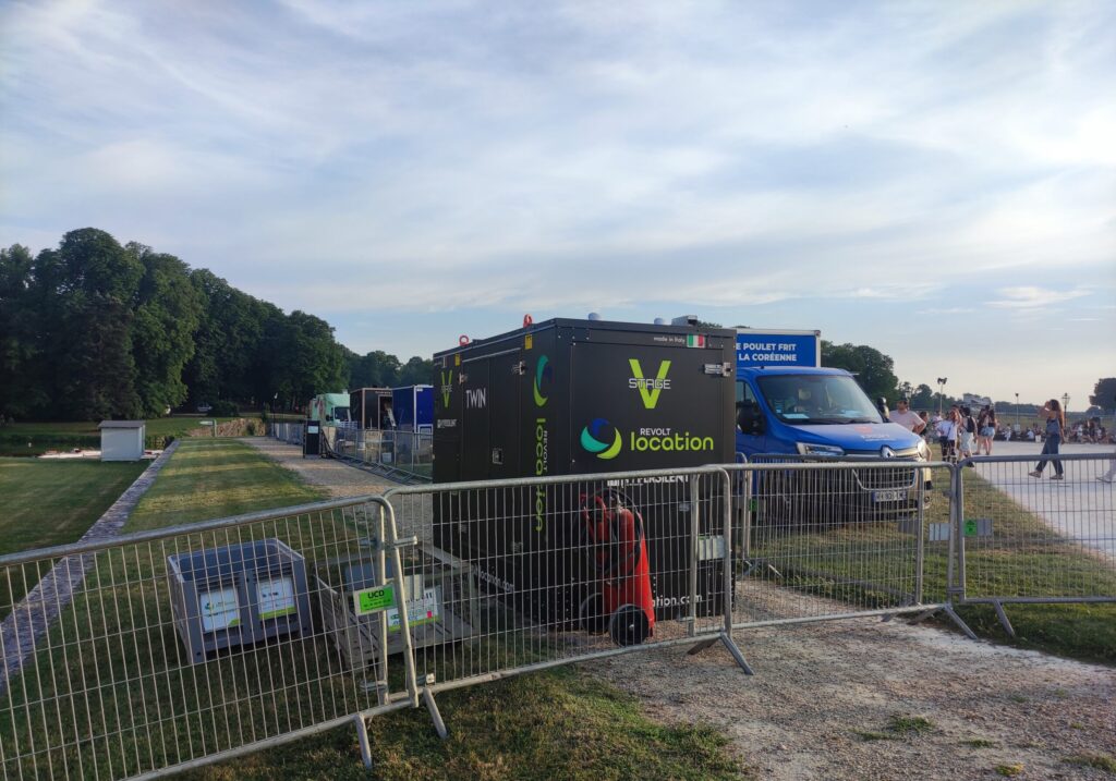 Groupe électrogène Stage V Twin floqué du logo Revolt Location, installé en zone technique sécurisée le long d'un canal en bord d'événement.