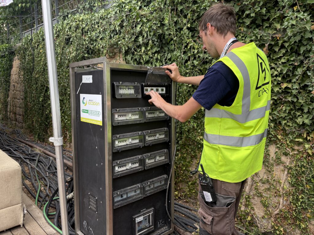 Intervenant en gilet haute visibilité contrôlant les disjoncteurs et compteurs d'une armoire électrique inox Revolt Location, en extérieur.