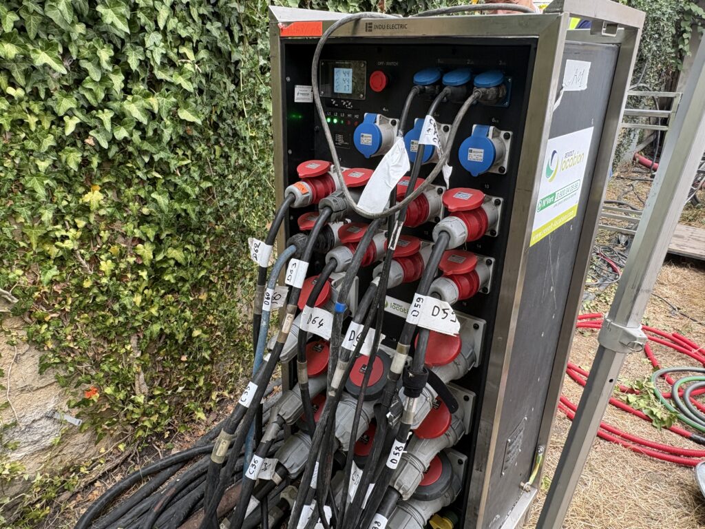 Armoire électrique Revolt Location à châssis inox, prises industrielles bleues et rouges avec câbles étiquetés, arrêt d'urgence et afficheur.