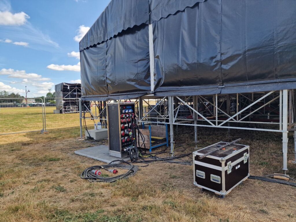 Installation électrique temporaire sous une scène événementielle avec coffret de distribution et câbles électriques