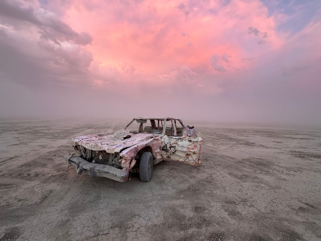 Ancienne voiture abandonnée sur un sol désertique sous un ciel aux couleurs rosées
