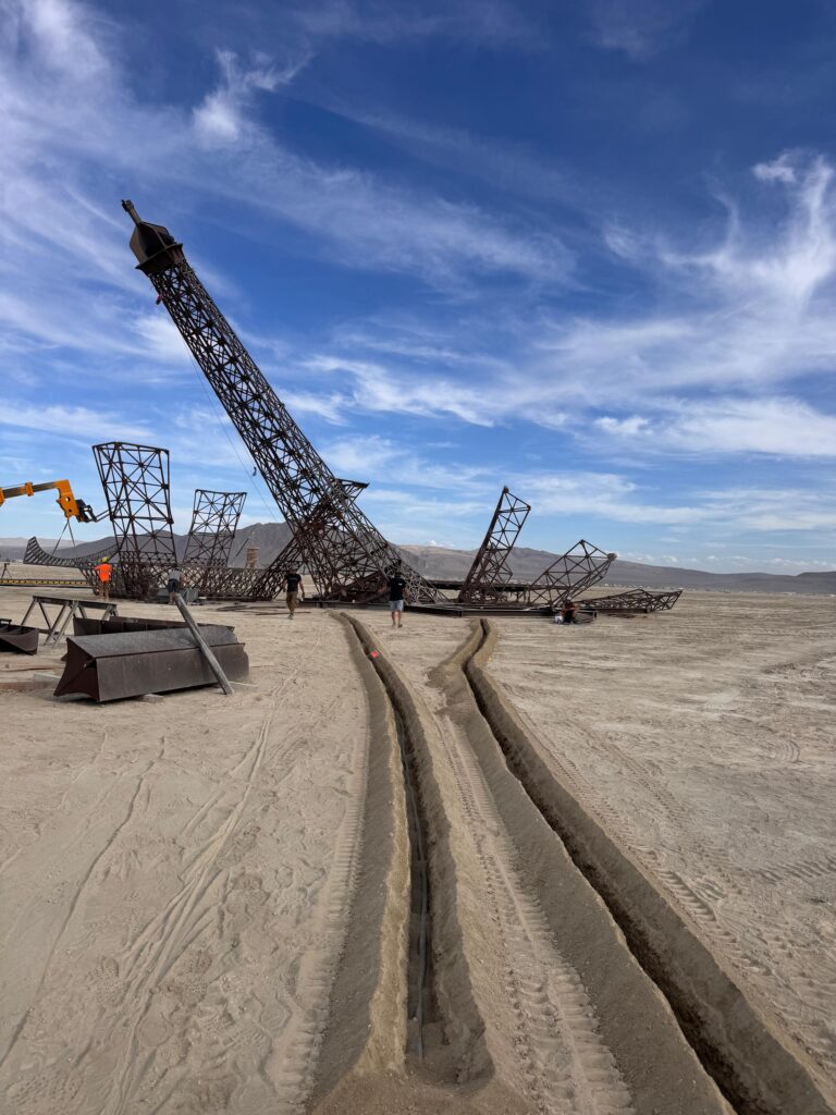 Installation temporaire en cours de montage sur un site événementiel désertique avec structures métalliques et tranchées techniques